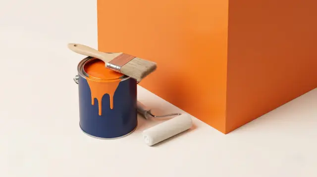 A navy paint tin of tangerine paint with a decorator's brush and roller on warm paper